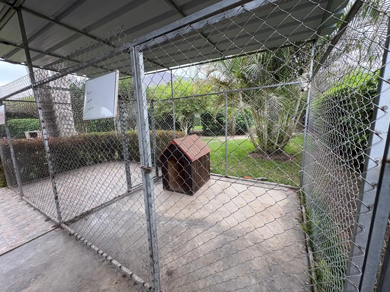 Canil techado con piso de cemento, casita de madera y salida directa al jardín de Petit Lodge